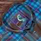 Blue plaid shirt with a logo patch on a wooden surface